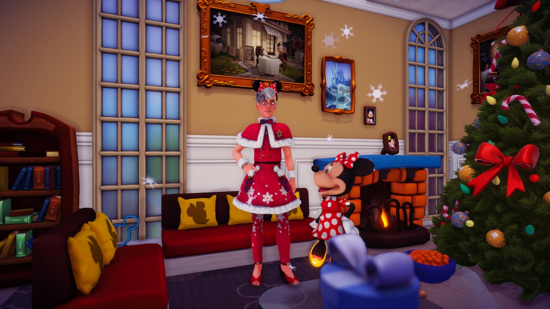 The player character and Minnie Mouse standing inside of a room with a Christmas tree to the side. The player is wearing a red dress with a white fur trim at the bottom and winter motives on its skirt, with matching red tights and boldero. On his feet are red open-toe heels. Minnie's in her signature red dress with polka-dots. They are wearing matching bows with polka-dots. Snowflakes are falling from the ceiling.