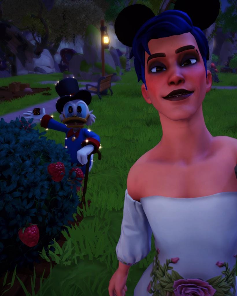 A selfie of the player character and Scrooge McDuck. The player has a masculine body frame, blue hair, and is wearing a white gown with floral details on the waist. They are also wearing black eyeshadow and black lipstick.