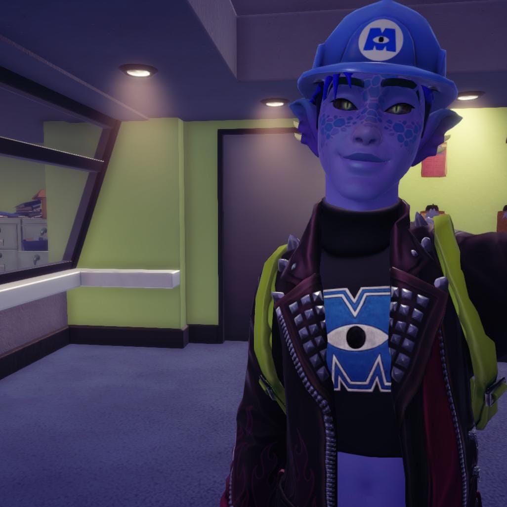 A selfie of the player character in the Monsters Inc. realm. He has blue skin with dark blue markings on his face, blue fin-like ears, and cat-like eyes. He is wearing the blue Monsters Inc. helmet, a black crop top with a Monsters Inc. logo and a leather jacket with spikes.
